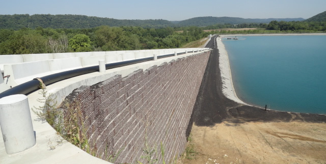 Concrete block retention wall forming one side of a large retention basin with a rolling-hill landscape in the background.